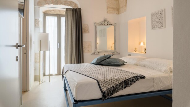 A bedroom with a bed, a mirror, a door, and a light fixture.