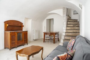 A living room with a sofa, wooden coffee table, and a dining table with chairs. A staircase with a patterned railing is visible in the background. - Casa Ibla Duplex con Terrazza by Wonderful Italy (Ragusa)