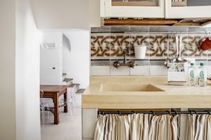 A kitchen with a beige countertop, a sink, and a patterned backsplash. There are clear chairs and a wooden table in the adjacent dining area. - Casa Ibla Duplex con Terrazza by Wonderful Italy (Ragusa)
