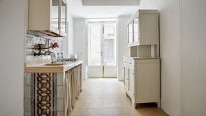 A narrow kitchen with a tiled backsplash, a gas stove, and a sink. There is a window with a view of the street. - Casa Ibla Duplex con Terrazza by Wonderful Italy (Ragusa)