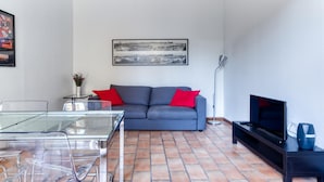 A modern living room with a grey sofa, red cushions, a glass coffee table, a TV, and a framed cityscape picture on the wall. - Castiglione Family Apartment by Wonderful Italy (Bologna)