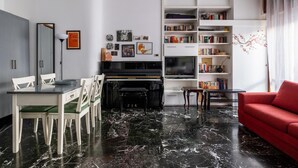 Ein Wohnzimmer mit einem Klavier, einem roten Sofa, einem Essbereich mit Stühlen und einer Bücherwand voller Bücher.