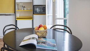 A modern kitchen with a round dining table, a hanging pendant light, a microwave, and a window with a view of the city.