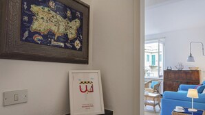 A framed map of Italy, a framed welcome sign, a wooden boat, and a wicker side table with a lamp and book.