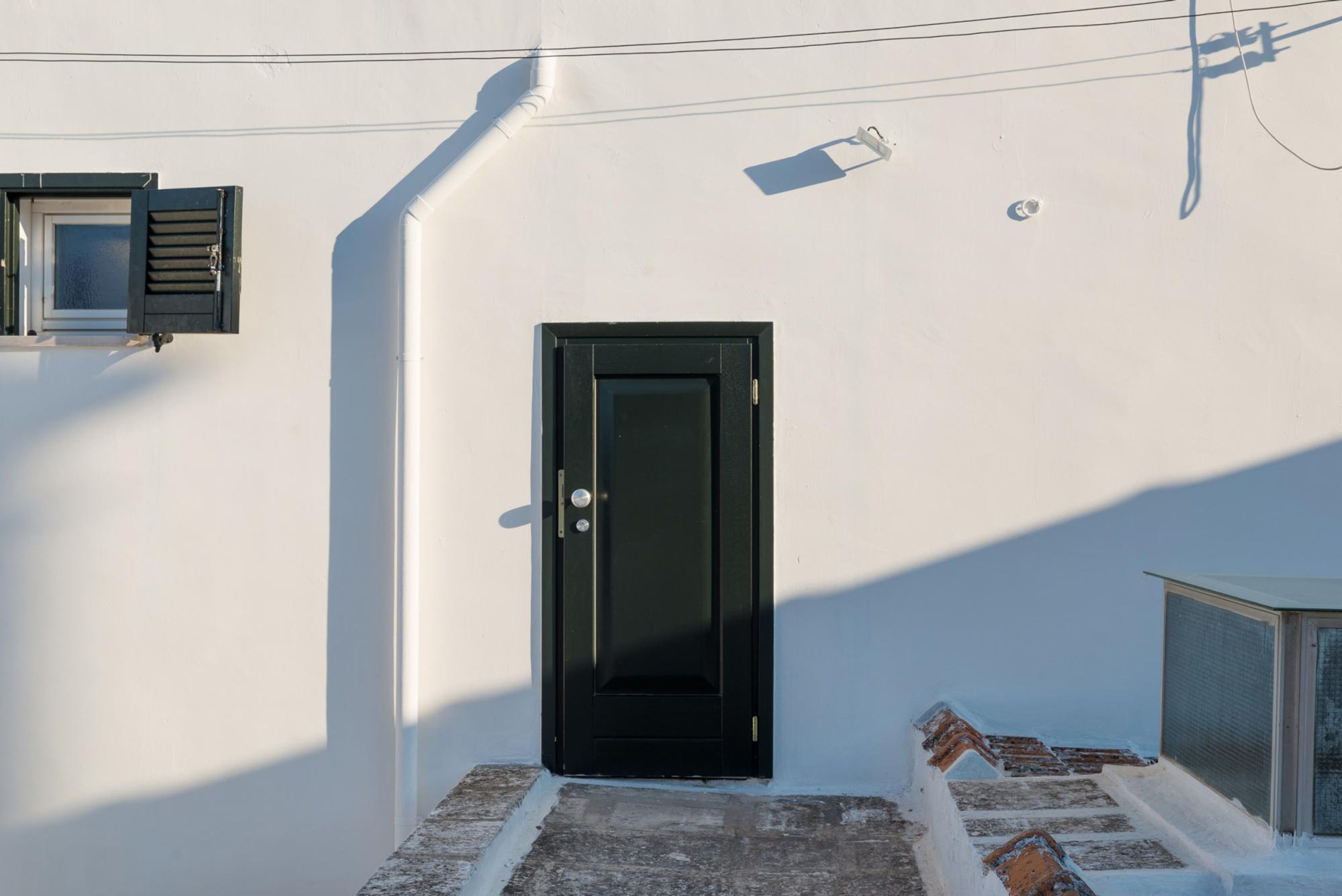 A black door with a small window above it, a white wall, and a small outdoor area with steps.