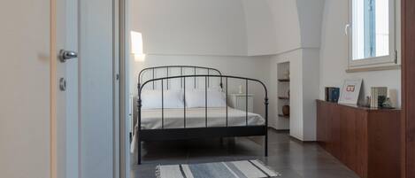 A bedroom with a bed, a nightstand, a wooden dresser, and a window.