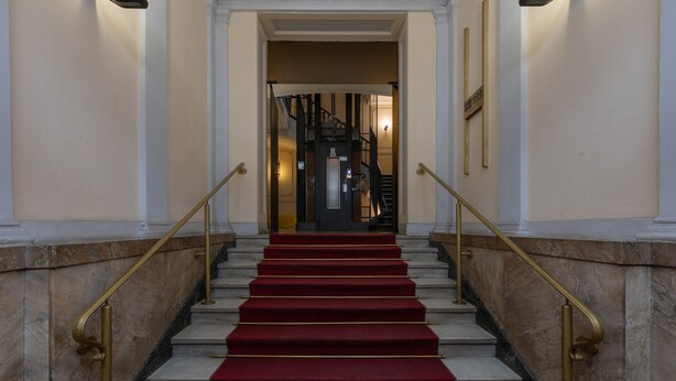 Un magnifique escalier, avec des murs en marbre et des marches recouvertes de moquette rouge, menant à un intérieur sombre.