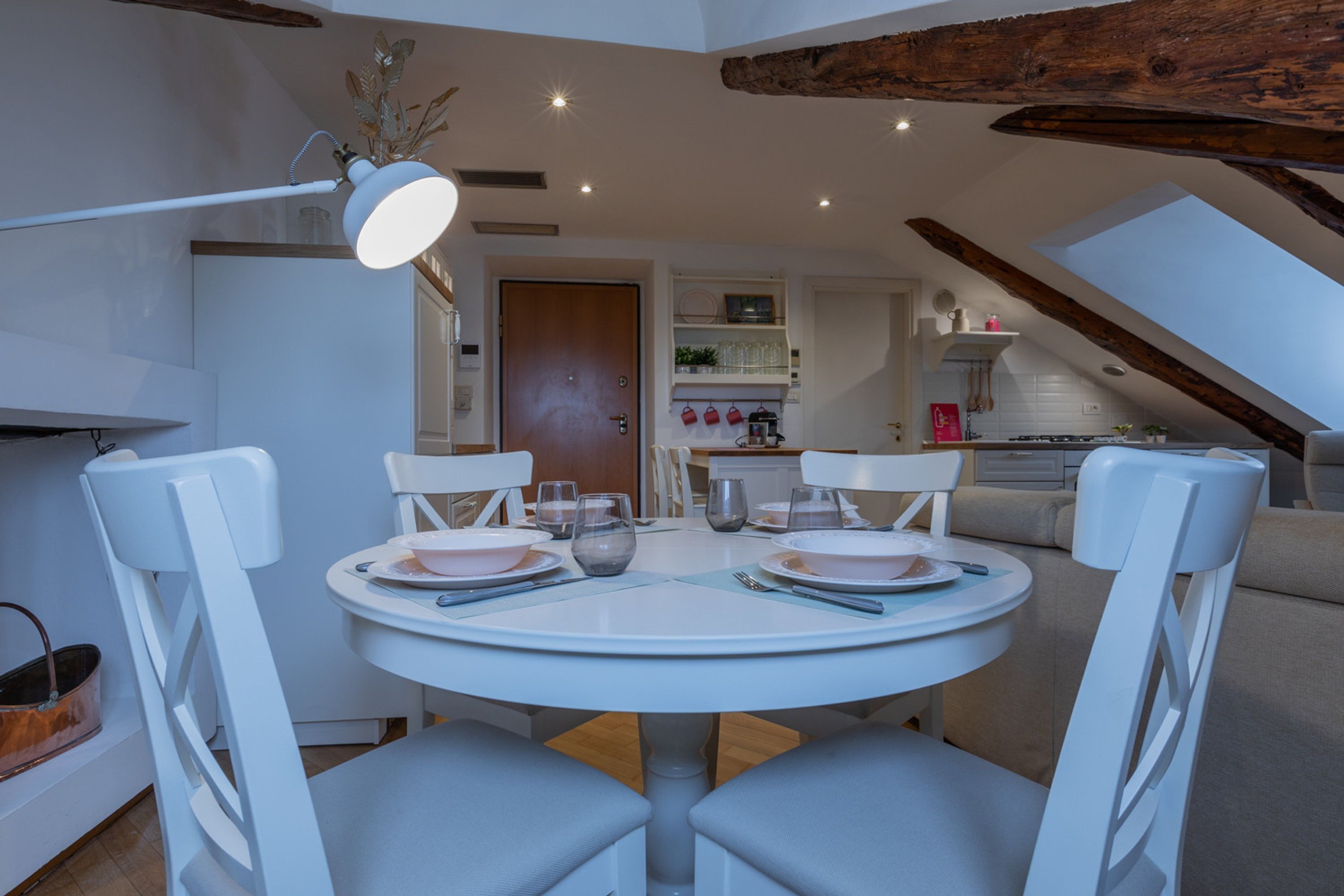 A dining area with a round table, white chairs, and a ceiling with exposed beams.