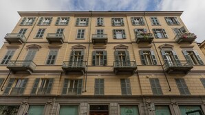 Un immeuble à plusieurs étages, de style architectural classique, doté de balcons avec des garde-corps, de grandes fenêtres et d’une entrée centrale avec une porte en bois.