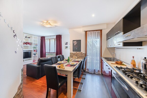 Eine moderne Küche mit Gasherd, ein Essbereich mit Tisch und Stühlen sowie ein Wohnzimmer mit Sofa und Fernseher.