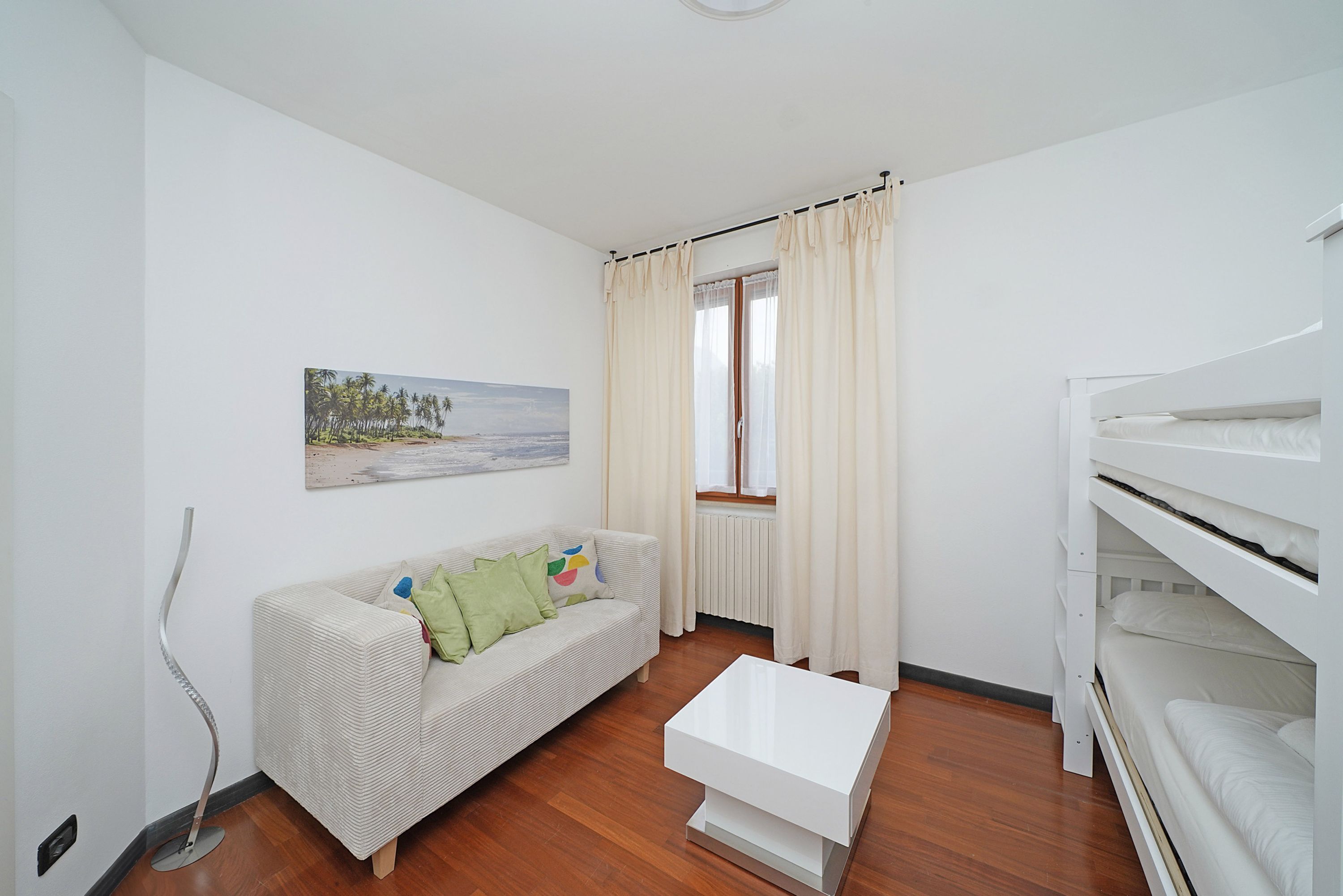 A room with a white sofa, a white coffee table, a bunk bed, and a window with curtains.