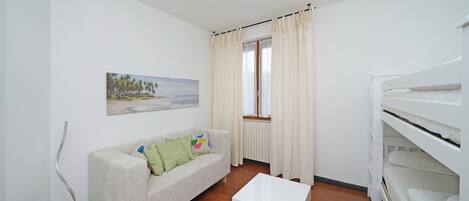 A room with a white sofa, a white coffee table, a bunk bed, and a window with curtains.