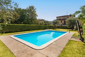 Ein rechteckiger Pool mit Fliesenrand, umgeben von einem gepflegten Rasen und Hecken.
