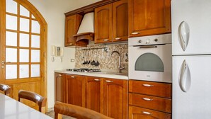 A kitchen with wooden cabinets, a white refrigerator, a stove, and a dining table with chairs. - Ortigia Seafront Apartment by Wonderful Italy (Syracuse)