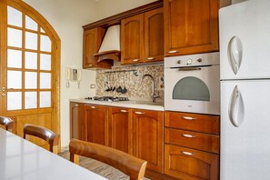 Eine Küche mit Holzschränken, einem weißen Kühlschrank, einem Herd und einem Esstisch mit Stühlen.