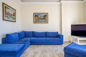 Ein Wohnzimmer mit einem blauen Modulsofa, einem weißen Fernsehschrank und zwei Bildern an der Wand.