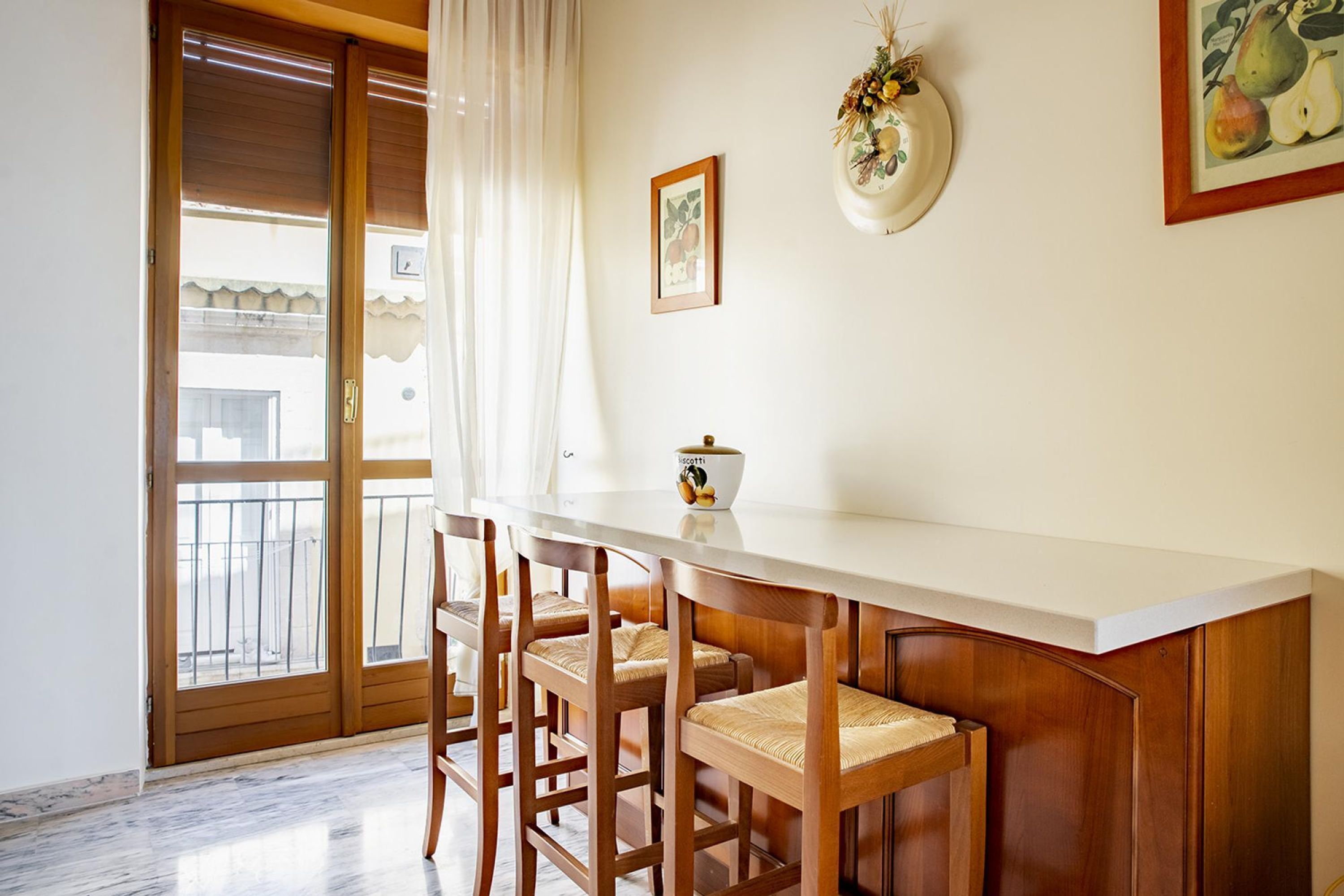 Ein Essbereich mit Holztisch und Stühlen, einer weißen Arbeitsplatte und Blick durch eine Glastür auf einen Balkon.