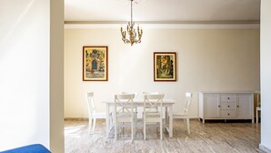 A dining area with a marble floor, white table and chairs, two framed artworks, and a chandelier. - Ortigia Seafront Apartment by Wonderful Italy (Syracuse)