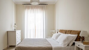 A bedroom with a bed, a nightstand, a chair, and a window with curtains. - Ortigia Seafront Apartment by Wonderful Italy (Syracuse)