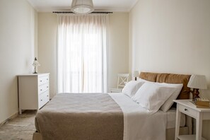 Ein Schlafzimmer mit einem Bett, einem Nachttisch, einem Sessel und einem Fenster mit Vorhängen.