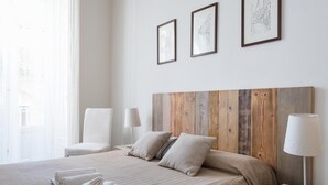 A hotel room with a large bed, a wooden headboard, two bedside lamps, a chair, and a window with sheer curtains. - Appartamento di Stile a Ortigia by Wonderful Italy (Syracuse)
