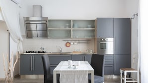 A compact kitchen with grey cabinets, a white table, and a small dining area. - Appartamento di Stile a Ortigia by Wonderful Italy (Syracuse)