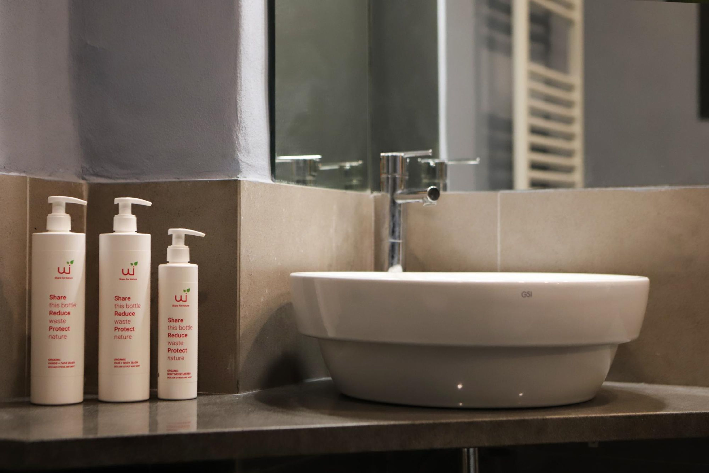 A bathroom with a white sink, three white bottles with pumps, and a mirror.