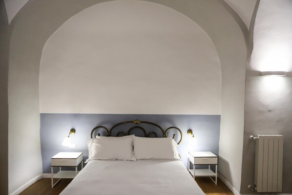 A bedroom with a large arched ceiling, a bed with white linens, two bedside tables with lamps, and a radiator. - Il Loggiato - Appartamento Luna by Wonderful Italy (Naples)