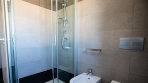 A modern bathroom with a glass-enclosed shower, a bidet, and a toilet.