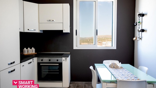 A compact kitchen with white cabinets, a built-in oven, and a window with a view of a landscape.