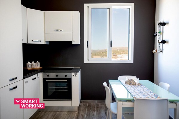 A compact kitchen with white cabinets, a built-in oven, and a window with a view of a landscape. - Le Terrazze sui Tetti di Noto by Wonderful Italy (Noto)