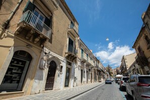 A street with historic buildings, a clear blue sky, and parked cars. - Le Terrazze sui Tetti di Noto by Wonderful Italy (Noto)