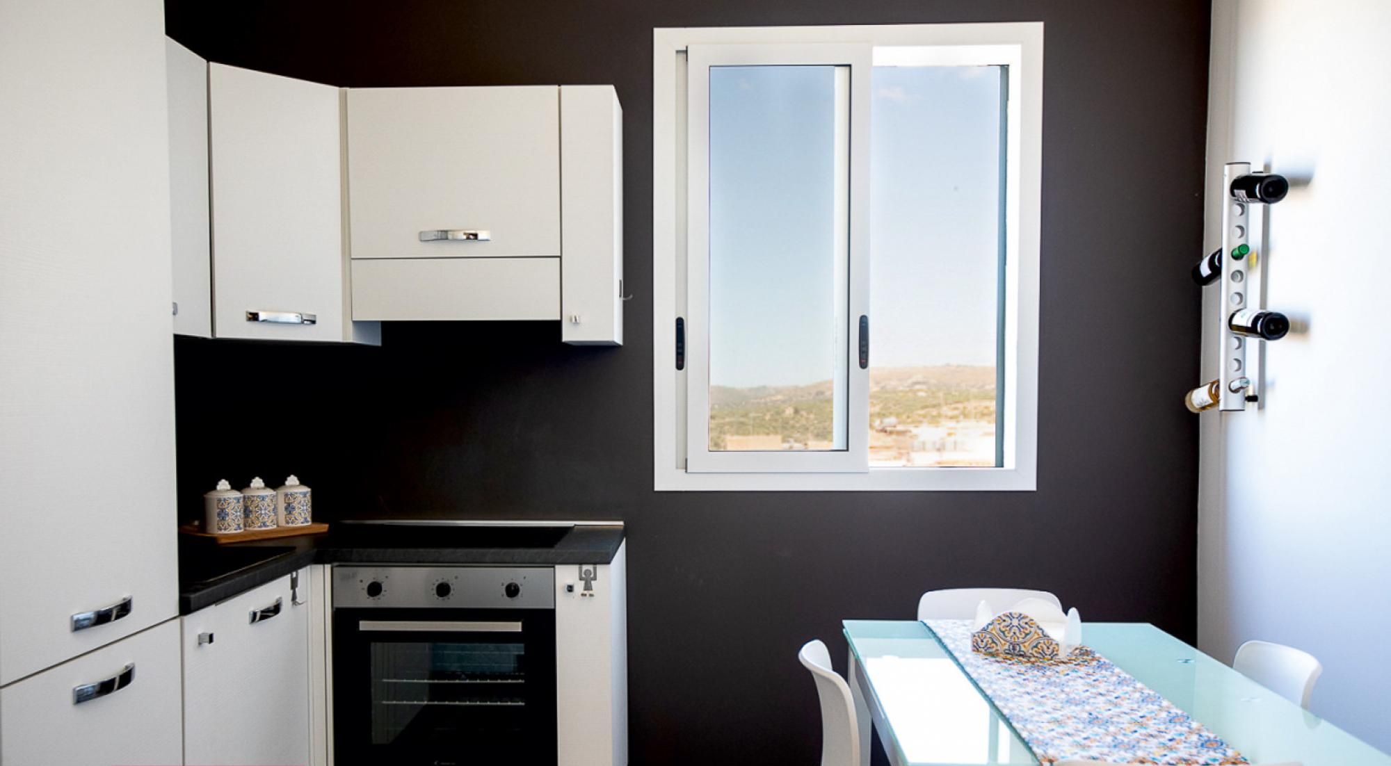 A compact kitchen with white cabinets, a built-in oven, and a window with a view of a landscape.