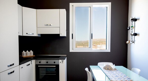 Une cuisine compacte avec des meubles blancs, un four encastré et une fenêtre donnant sur un paysage.