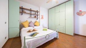 A bedroom with a bed, a wardrobe, a ceiling fan, and a shelf with decorative items. - Le Ortensie 1 Apartment by Wonderful Italy (Soiano del Lago)