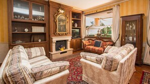 A traditional living room with a fireplace, two sofas, a bookshelf, and a television. - Le Ortensie 1 Apartment by Wonderful Italy (Soiano del Lago)