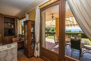 A room with a wooden cabinet, a sofa, and a view of an outdoor patio with a table and chairs. - Le Ortensie 1 Apartment by Wonderful Italy (Soiano del Lago)