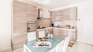 A modern kitchen with wooden cabinetry, a built-in oven, and a dining area with a glass table. - Le Corti Caterina B2 Apartment by Wonderful Italy (Lonato del Garda)