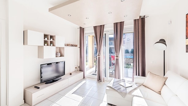 A modern living room with a flat-screen TV, a sofa, a coffee table, and a wall-mounted shelf with decorative items. - Le Corti Caterina B2 Apartment by Wonderful Italy (Lonato del Garda)