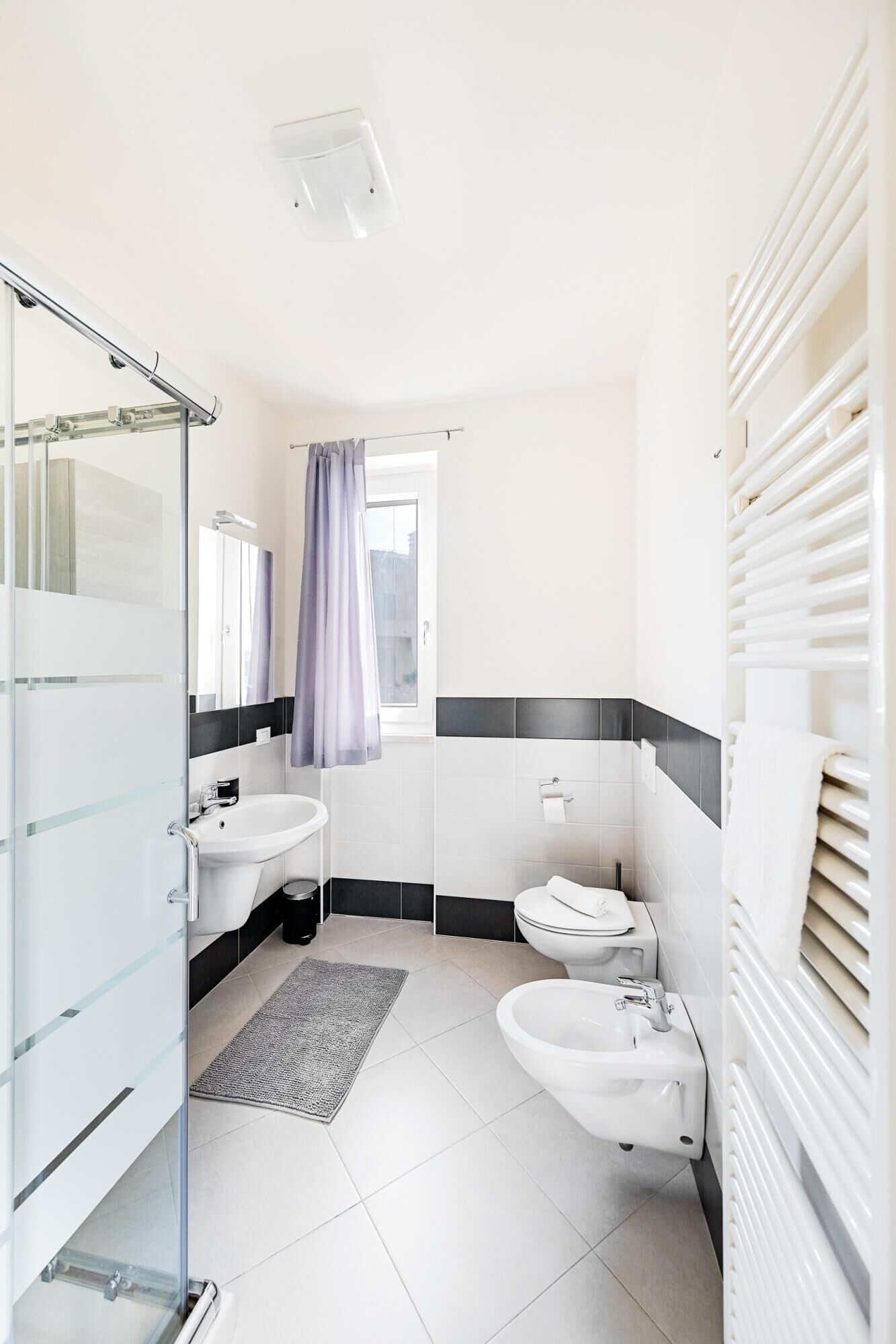 A modern bathroom with a glass shower enclosure, a sink, a toilet, and a bidet.