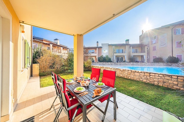An outdoor dining area with a table set for two, a pool, and a view of apartment buildings.