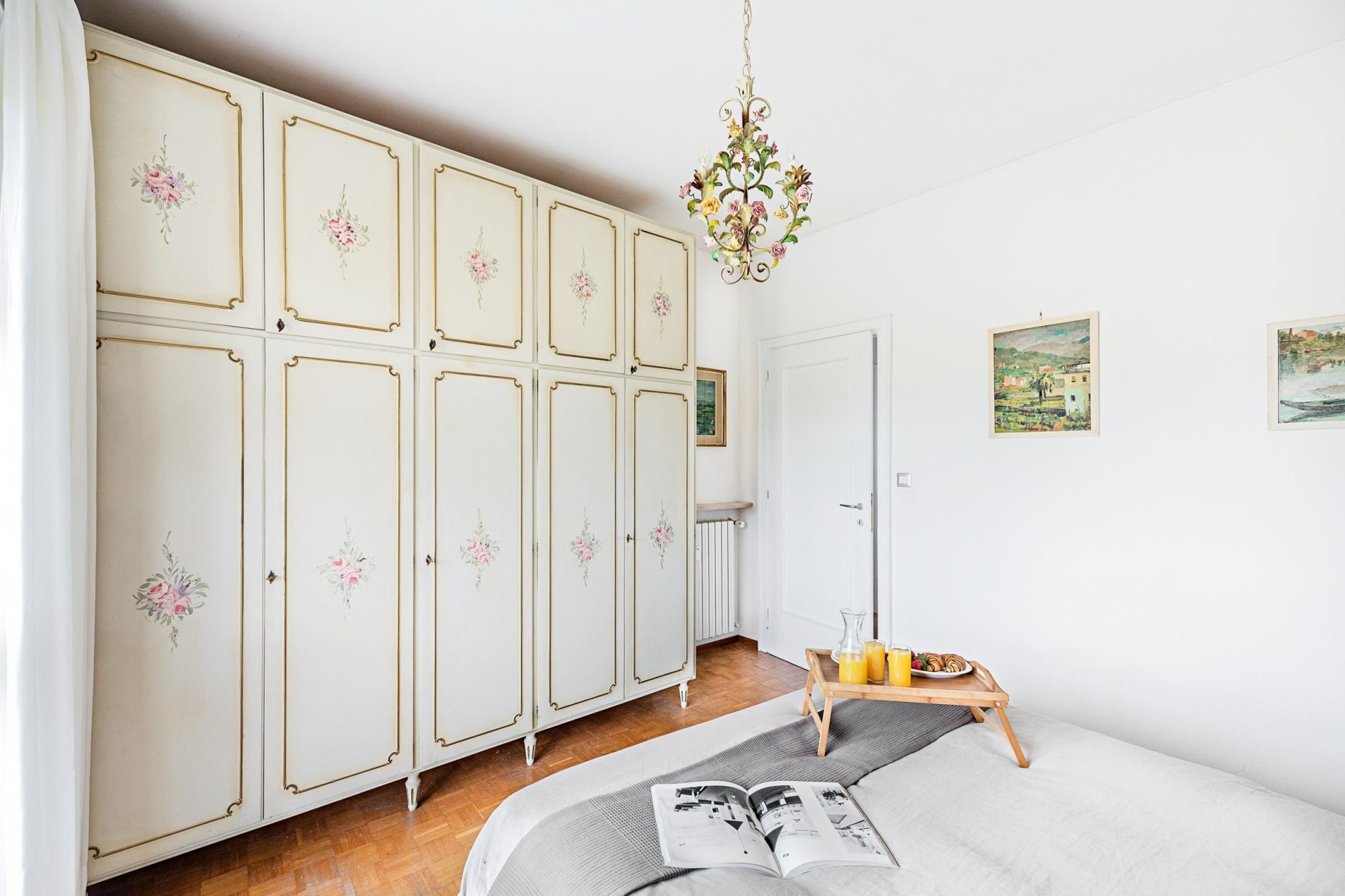Een slaapkamer met een bed, een dressoir, een radiator en een klein tafeltje met een dienblad.