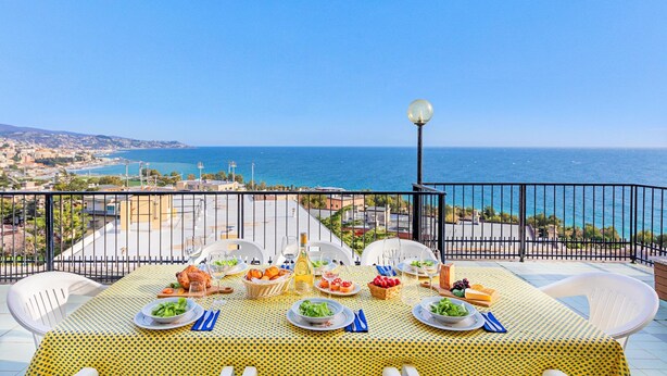 A dining table set with plates, glasses, and food on a balcony with a view of the sea. - Le Orchidee 19 by Wonderful Italy (Sanremo)