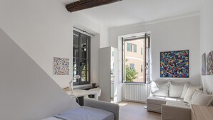 A modern bedroom with a bed, a desk, a sofa, and a window with a view of buildings.