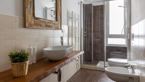 Ein modernes Badezimmer mit großem Spiegel, einem Aufsatzbecken, einem Standbecken, einer Duschkabine und einem Topf mit Pflanze.
