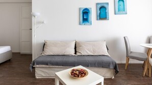 Ein modernes Wohnzimmer mit einer Couch, einem kleinen Tisch mit einer Schale und einem Sessel. An der Wand hängen drei gerahmte Kunstwerke.