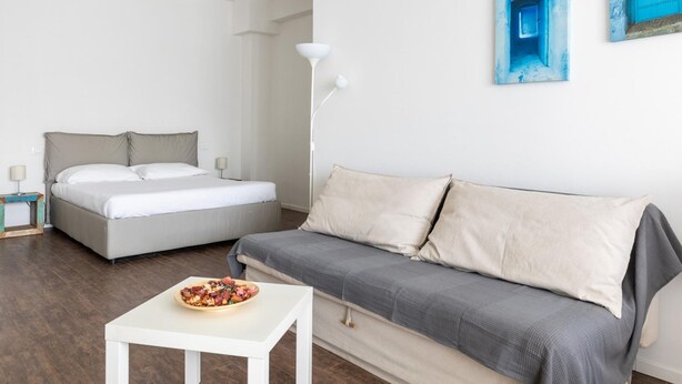 Ein Schlafzimmer mit einem Bett, einem grauen Sofa, einem weißen Tisch und einer Obstschale.
