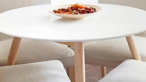 Ein runder, weißer Tisch mit einer Speisenplatte in der Mitte, umgeben von weißen Stühlen.