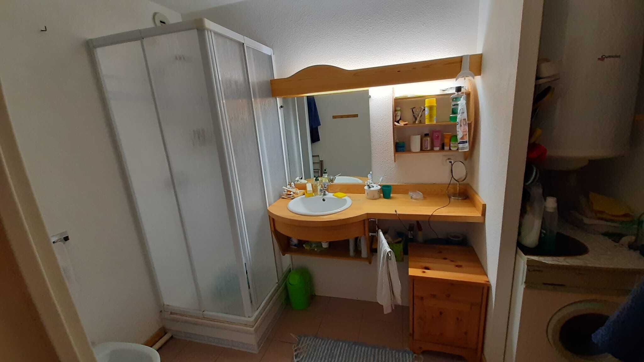 Une salle de bain avec une douche, un lavabo et un miroir. On y trouve une étagère avec des articles de toilette et un porte-serviettes.