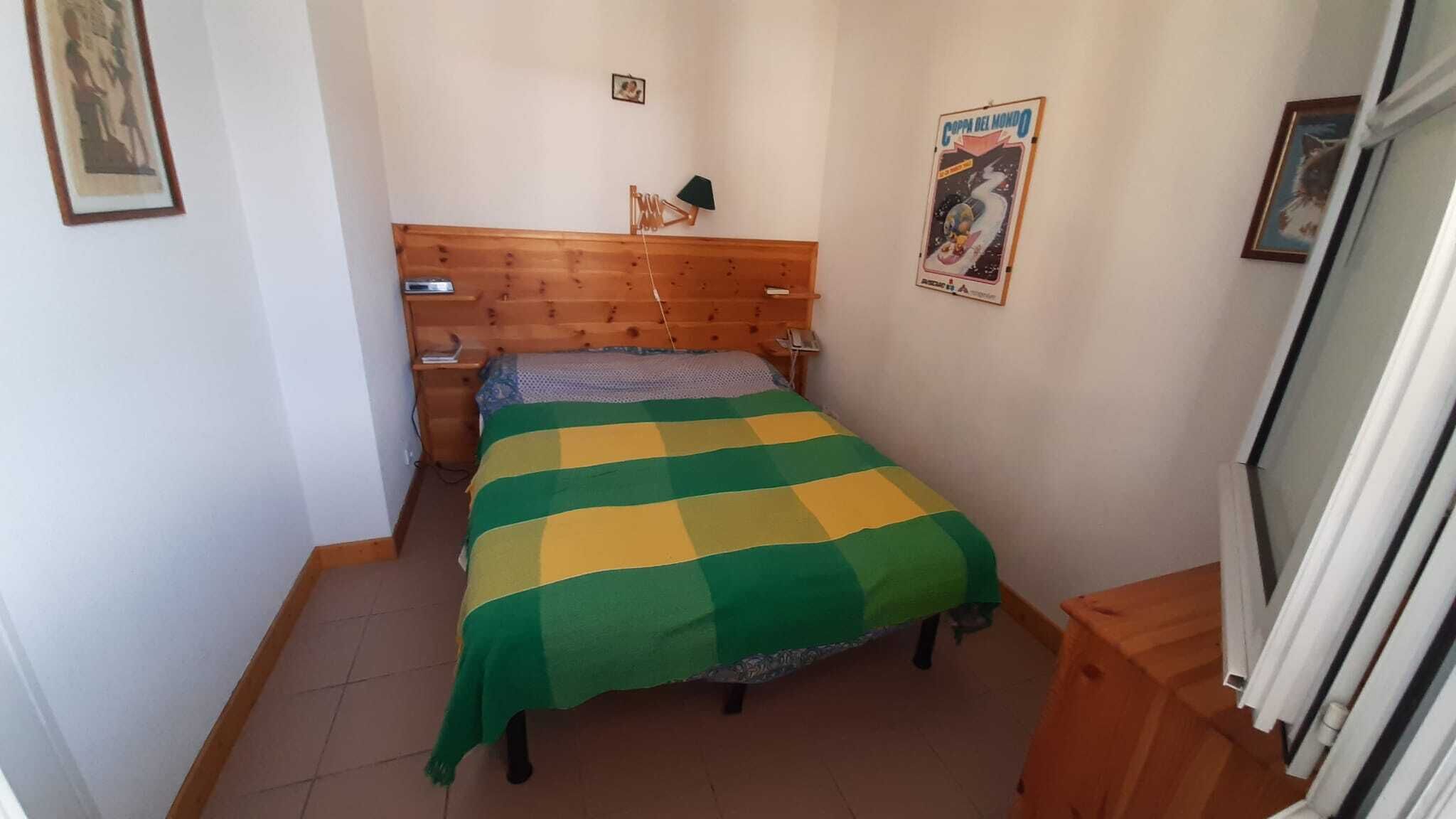 Une petite chambre à coucher, bien rangée, avec une tête de lit en bois, une couvre-lit à rayures et une affiche accrochée au mur.